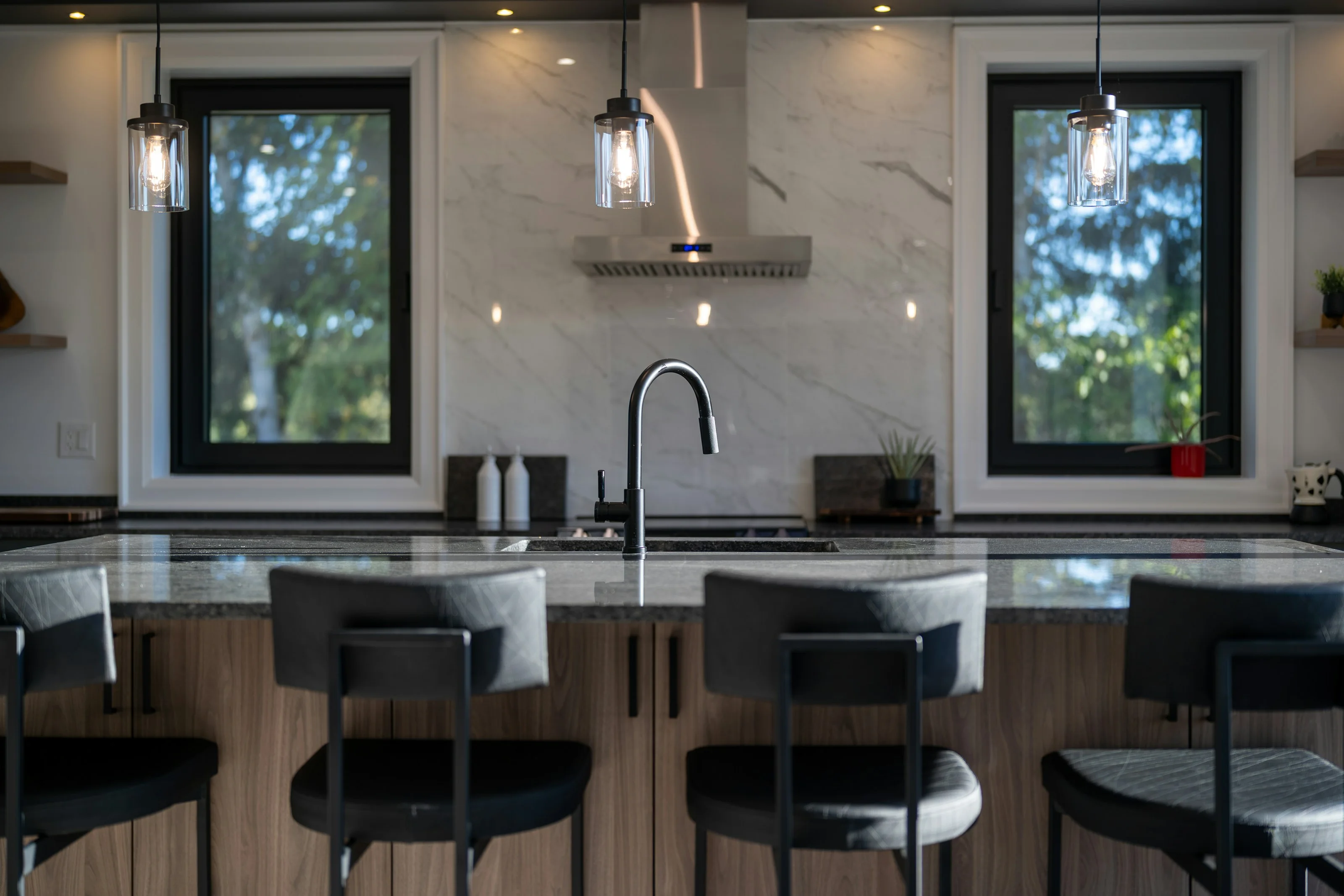 Granite kitchen island with bar stools, a matte black faucet and a marble slab backsplash