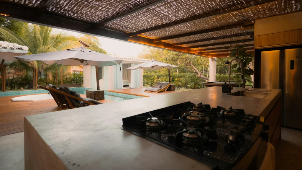 Outdoor kitchen with a stone countertop and cooktop beside a pool