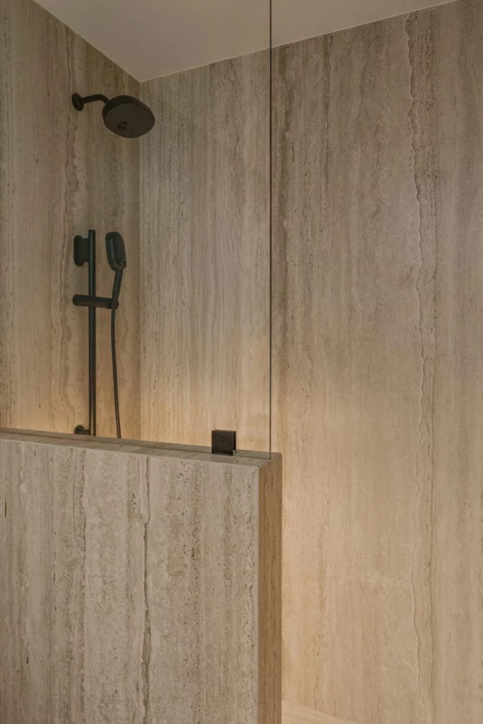 Full-slab vein-cut stone shower walls with black fixtures